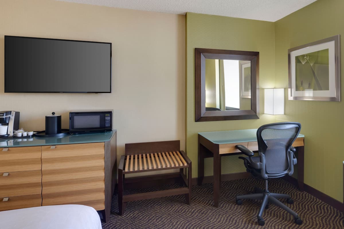 A hotel room with a bed, a desk with a chair, a television, a coffee maker, and a mirror.
