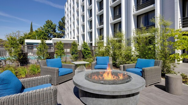 An outdoor seating area with wicker furniture and a central fire pit. - Holiday Inn San Jose - Silicon Valley by IHG (San Jose)