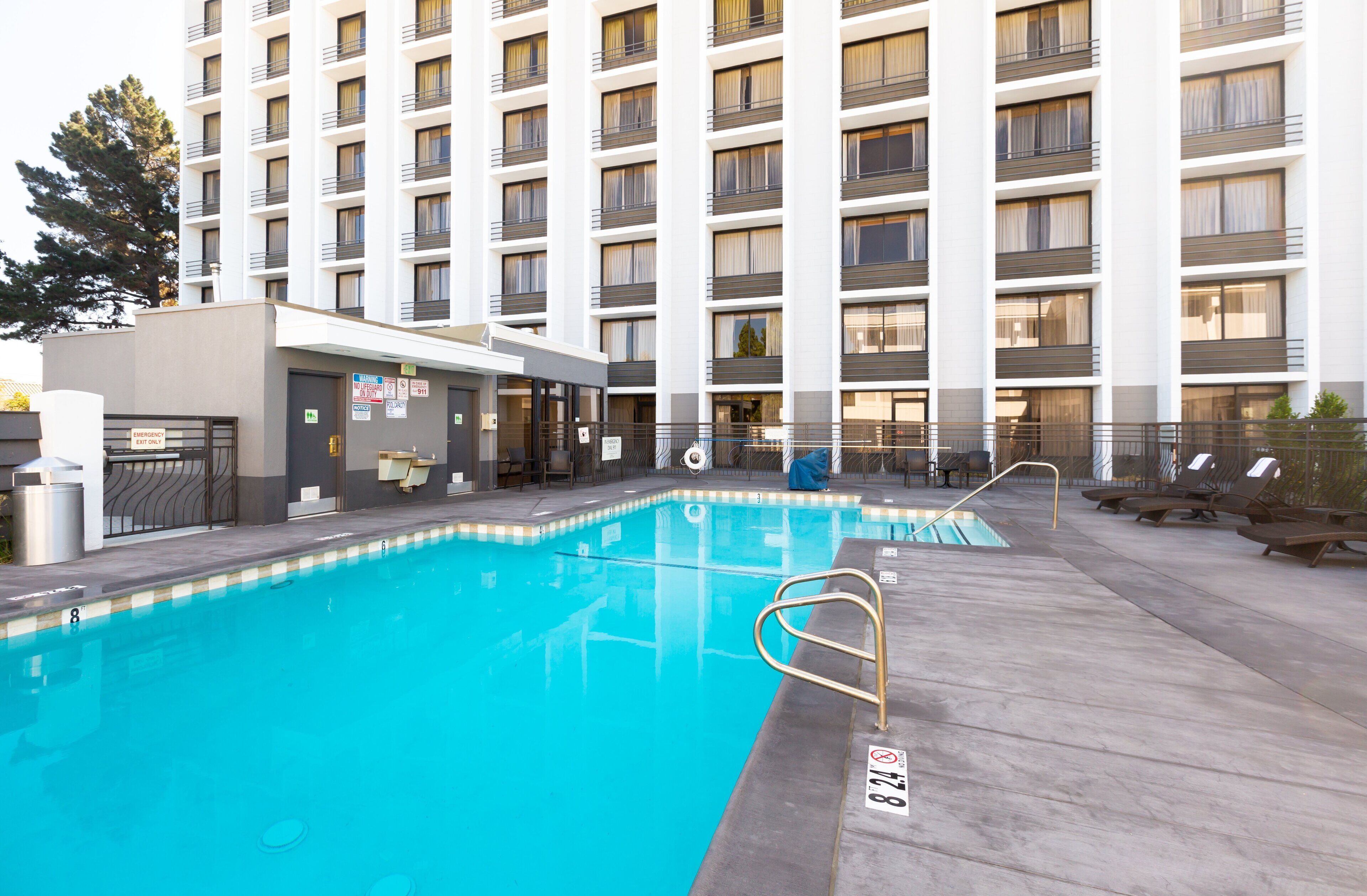 A swimming pool with a lifeguard chair, lounge chairs, and a building with multiple balconies in the background.