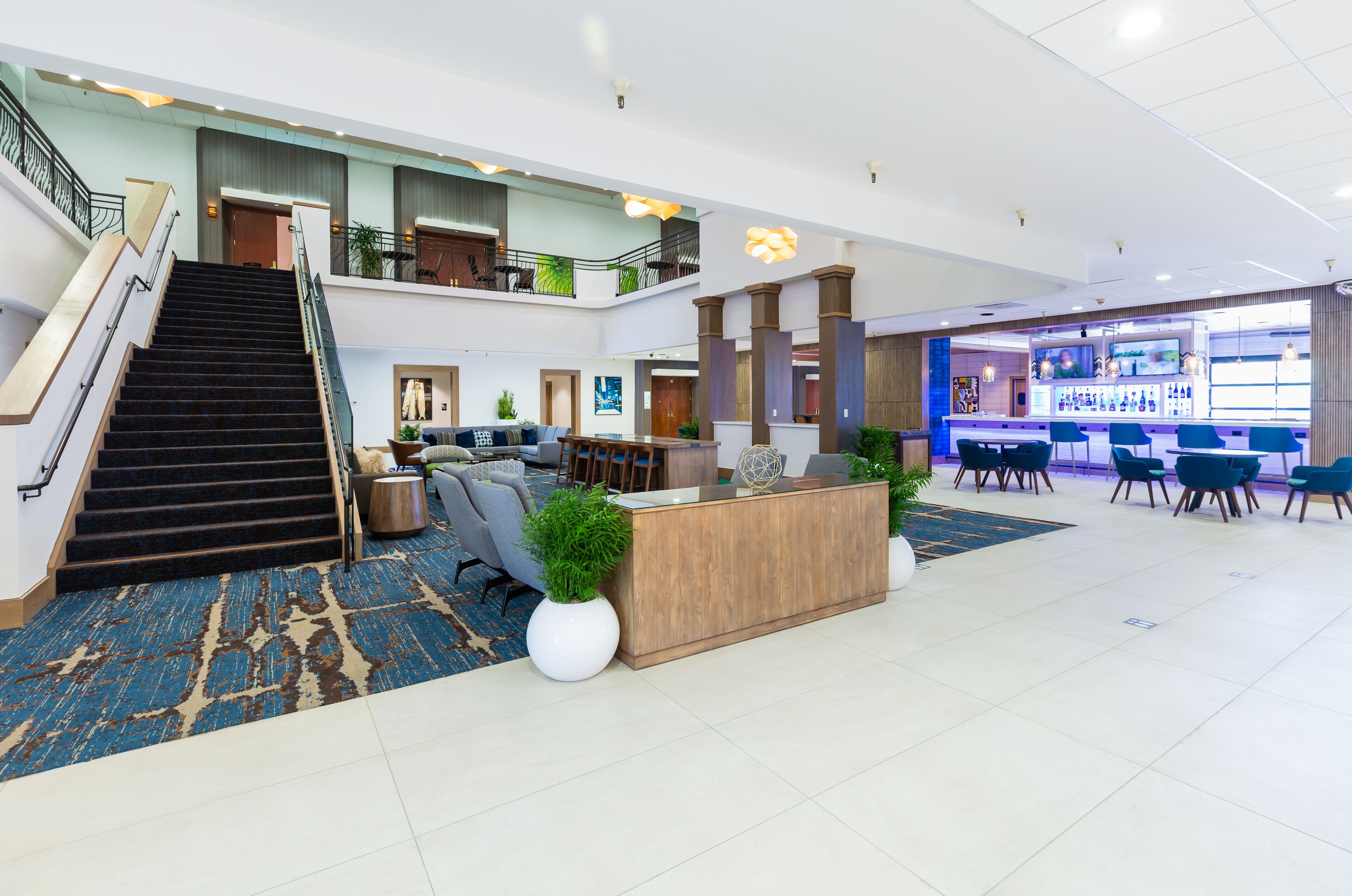 A spacious lobby with a reception desk, seating area, staircase, and a bar.