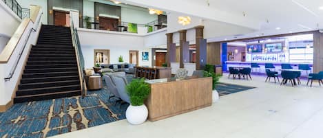 A spacious lobby with a reception desk, seating area, staircase, and a bar.