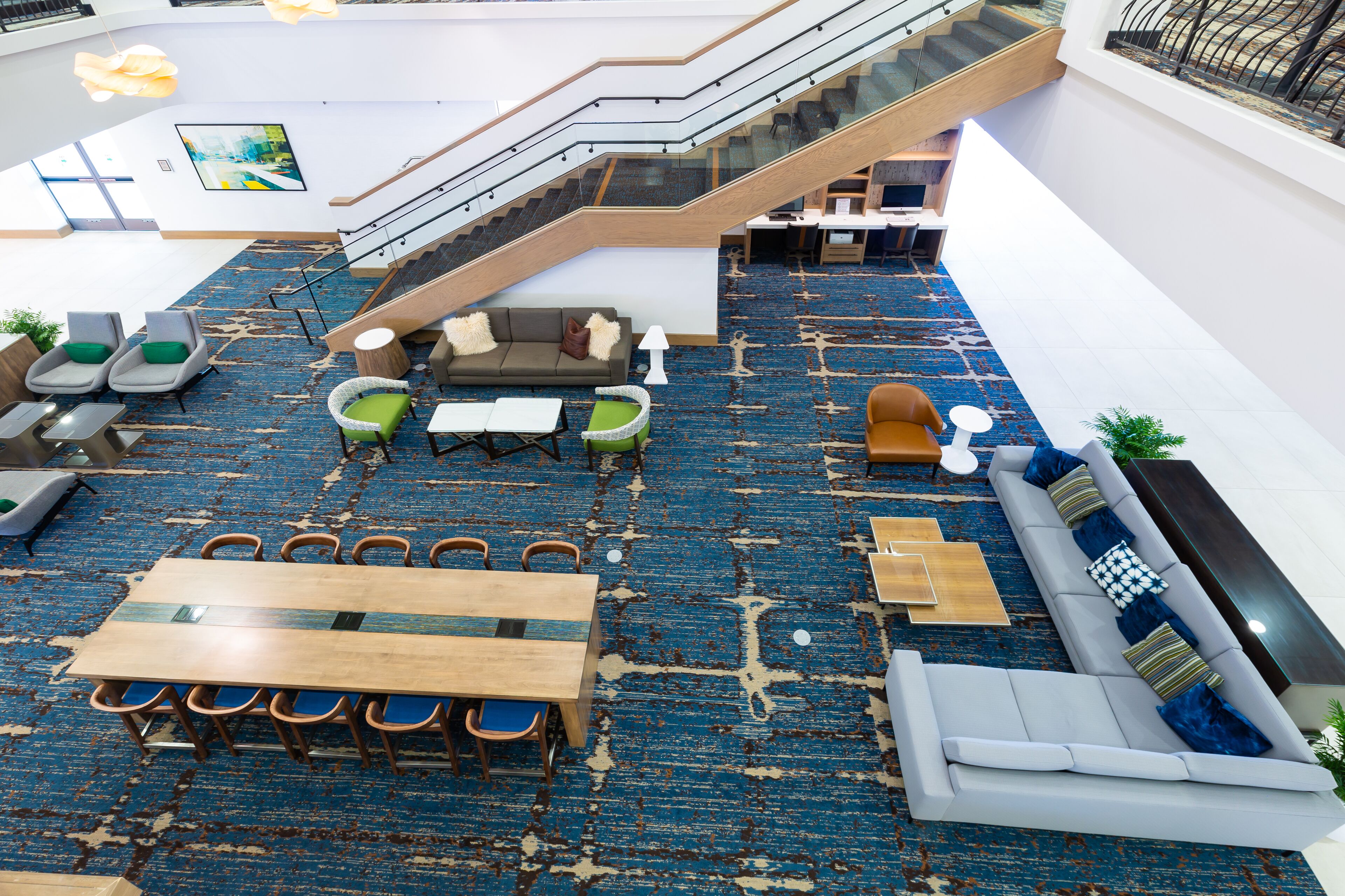 A spacious lobby with a blue carpet, a staircase, seating areas, and a large table.