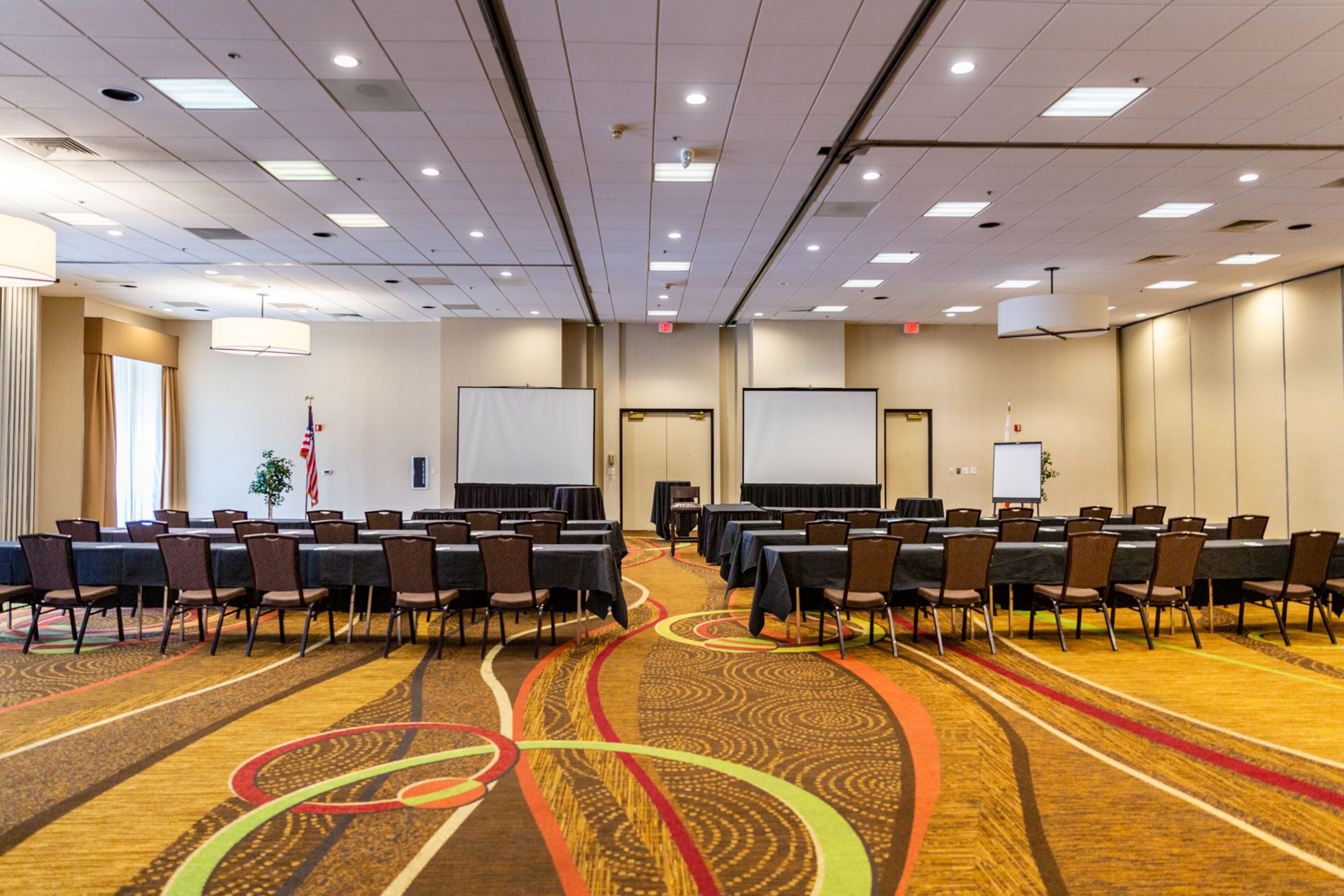 A conference room with rows of tables and chairs, a carpeted floor, and a whiteboard.
