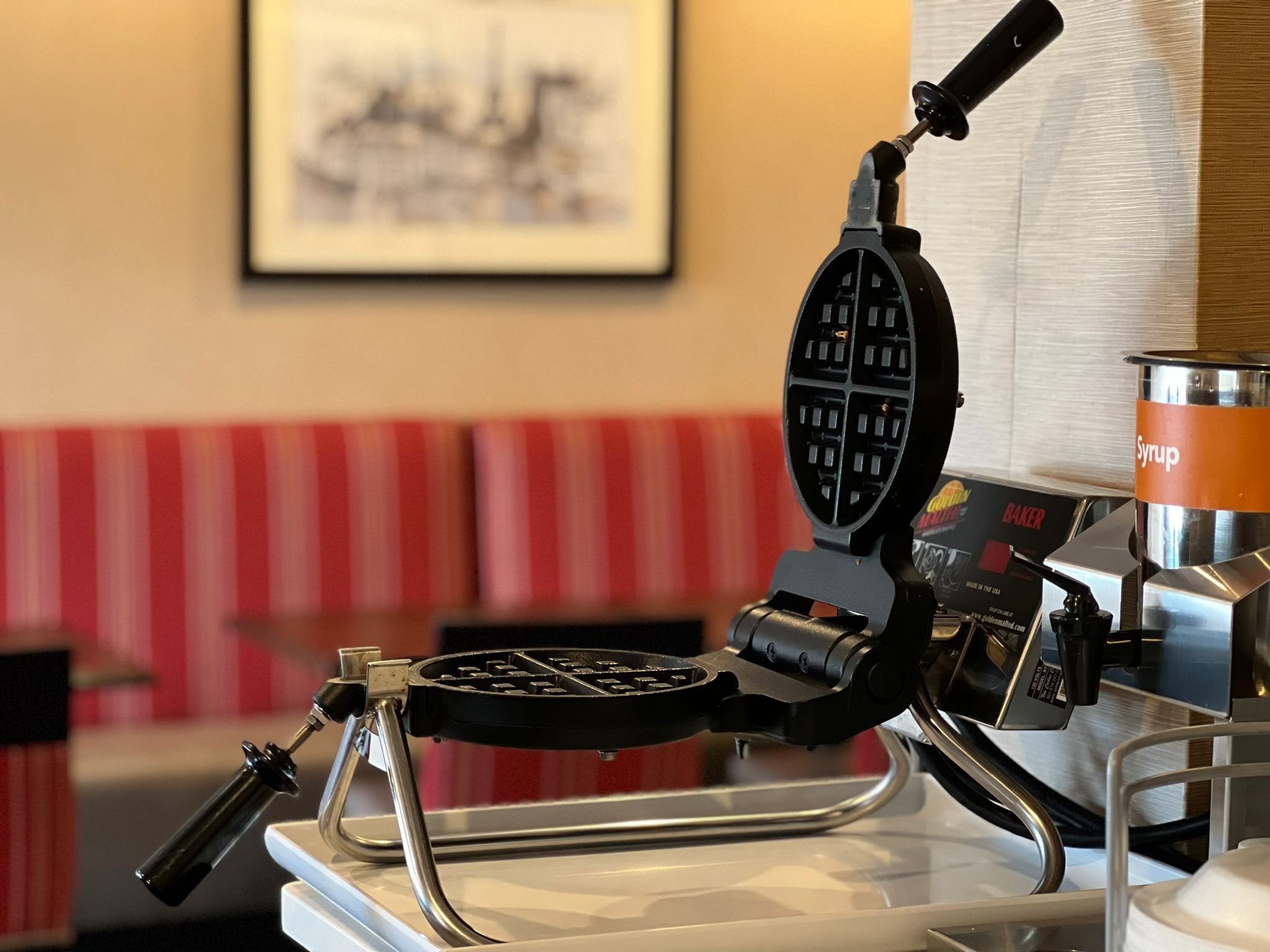 A waffle iron on a counter with a syrup container nearby.