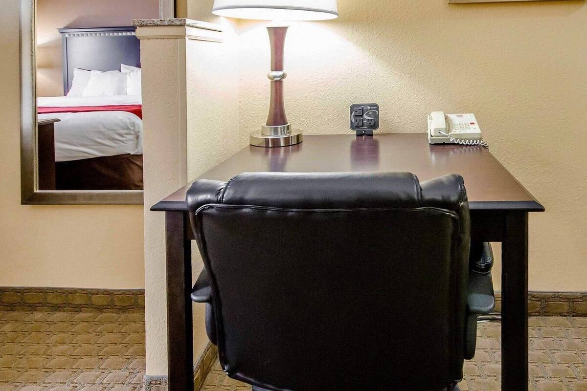 Ett hotellrum med ett skrivbord, en lampa, en telefon och en spegel som reflekterar en säng.
