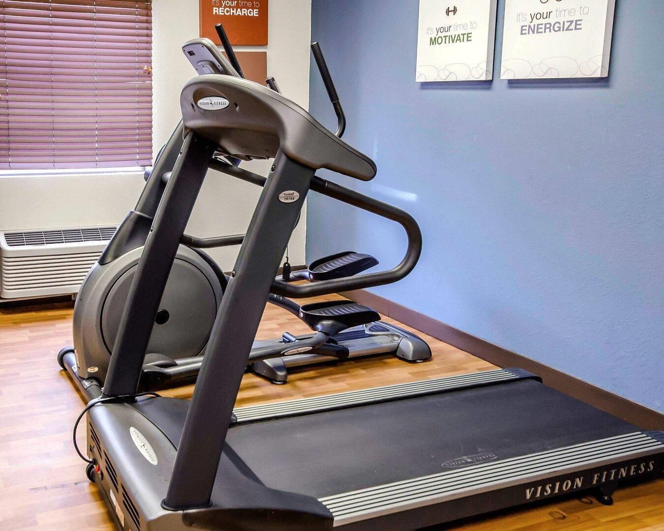 A treadmill in a fitness room with a wooden floor, a wall-mounted air conditioner, and motivational posters.