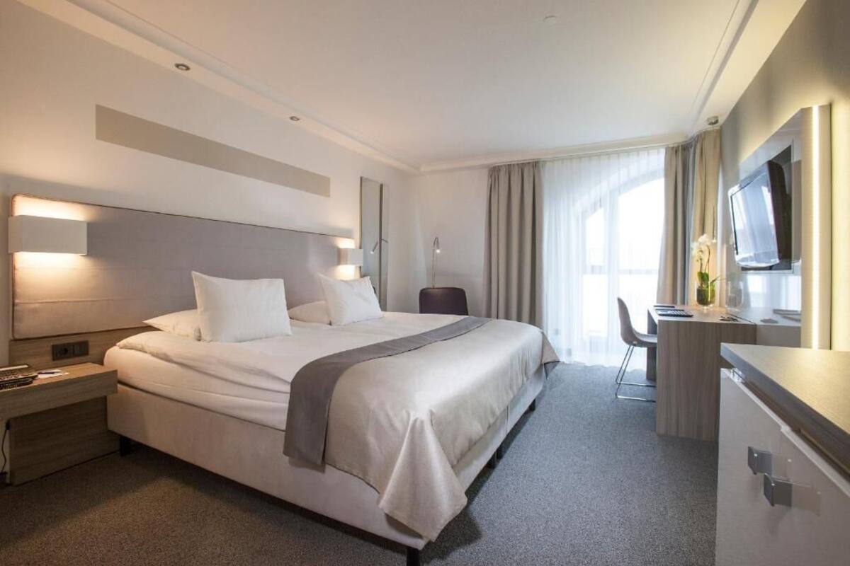 Une chambre d’hôtel moderne avec un grand lit, des tables de chevet, un bureau et une télévision.