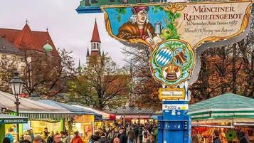 Una animada escena de mercado con un cartel destacado que anuncia el 'Münchner Reinheitsgebot' y un emblema tradicional de jarra de cerveza bávara.