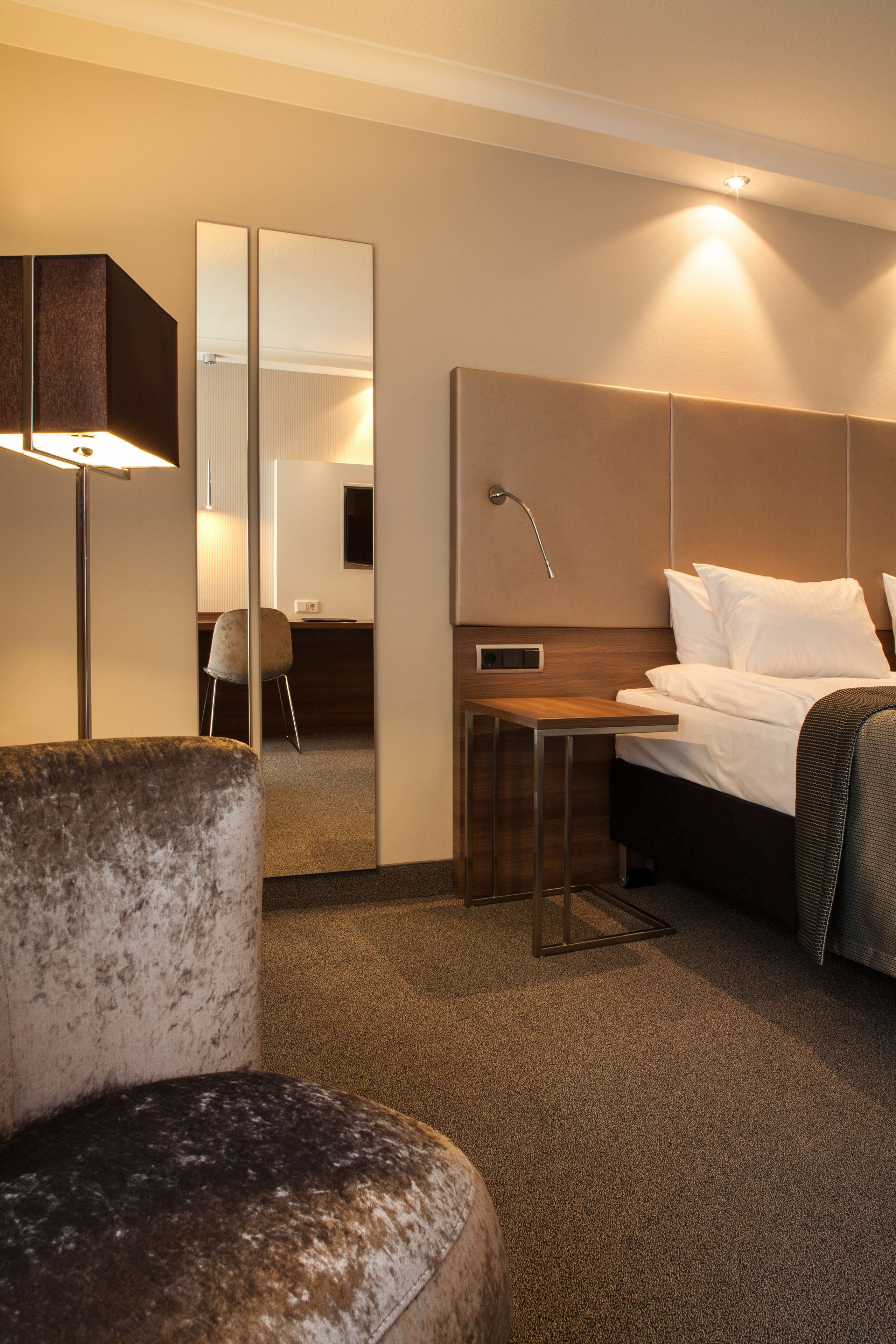 Una habitación de hotel con cama, escritorio, silla y un espejo grande.