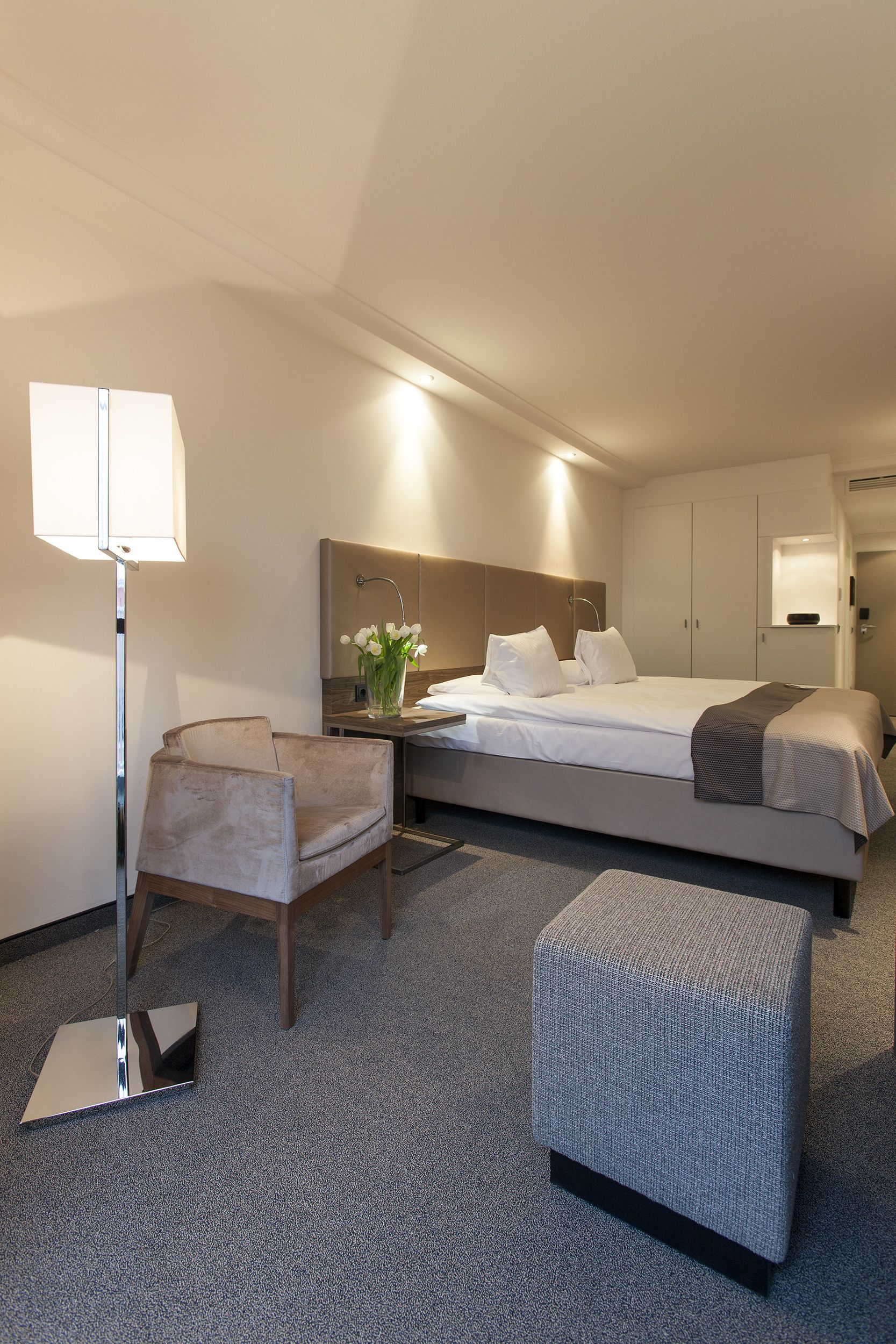 A hotel room with a bed, a chair, a desk, and a lamp.