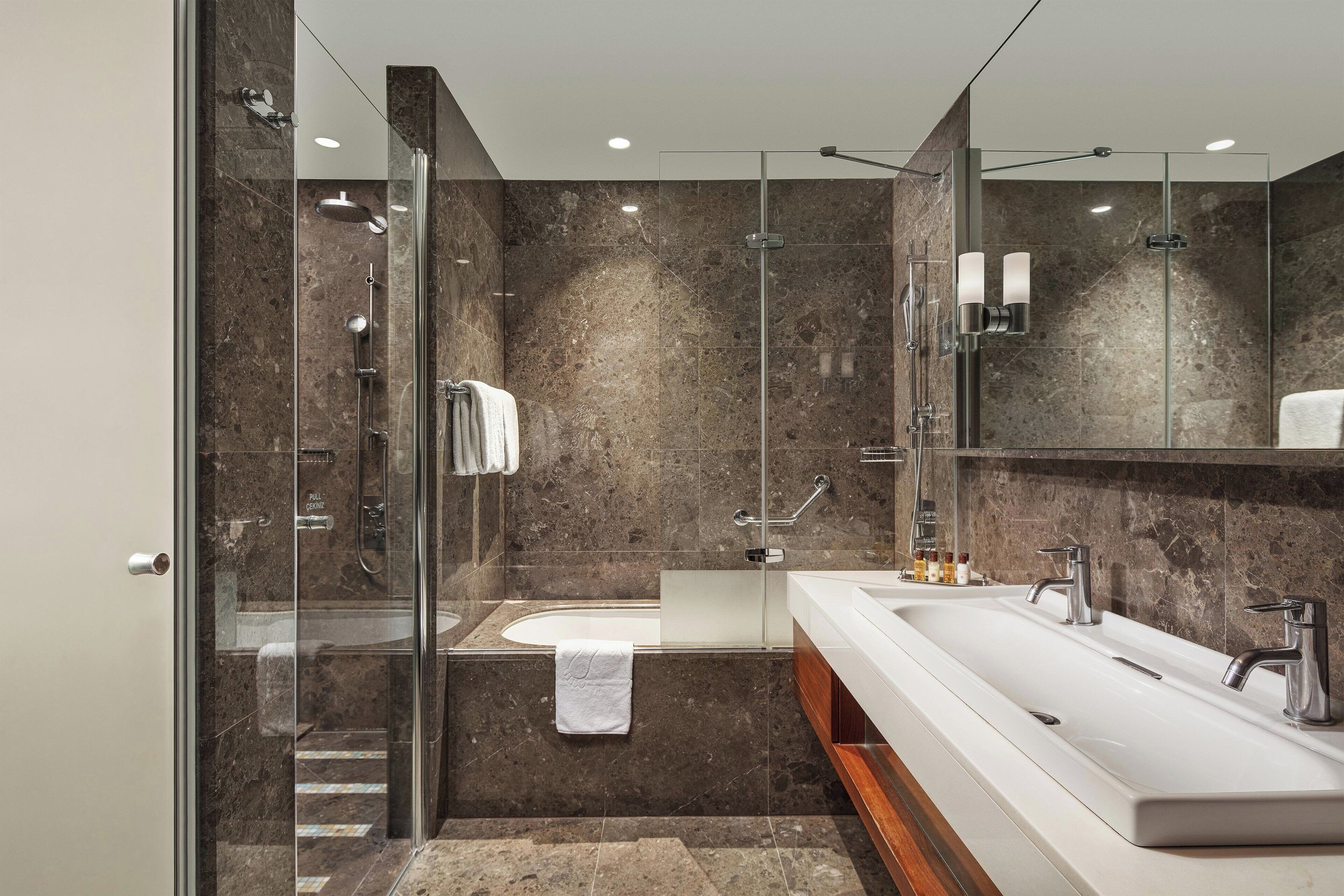 Ein modernes Badezimmer mit einer Glaskabine zur Dusche, einem großen weißen Waschbecken und einer Wand mit Marmorfliesen.