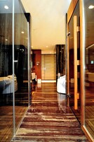Un baño de hotel moderno con ducha de vidrio, tocador de madera y piso de mármol.