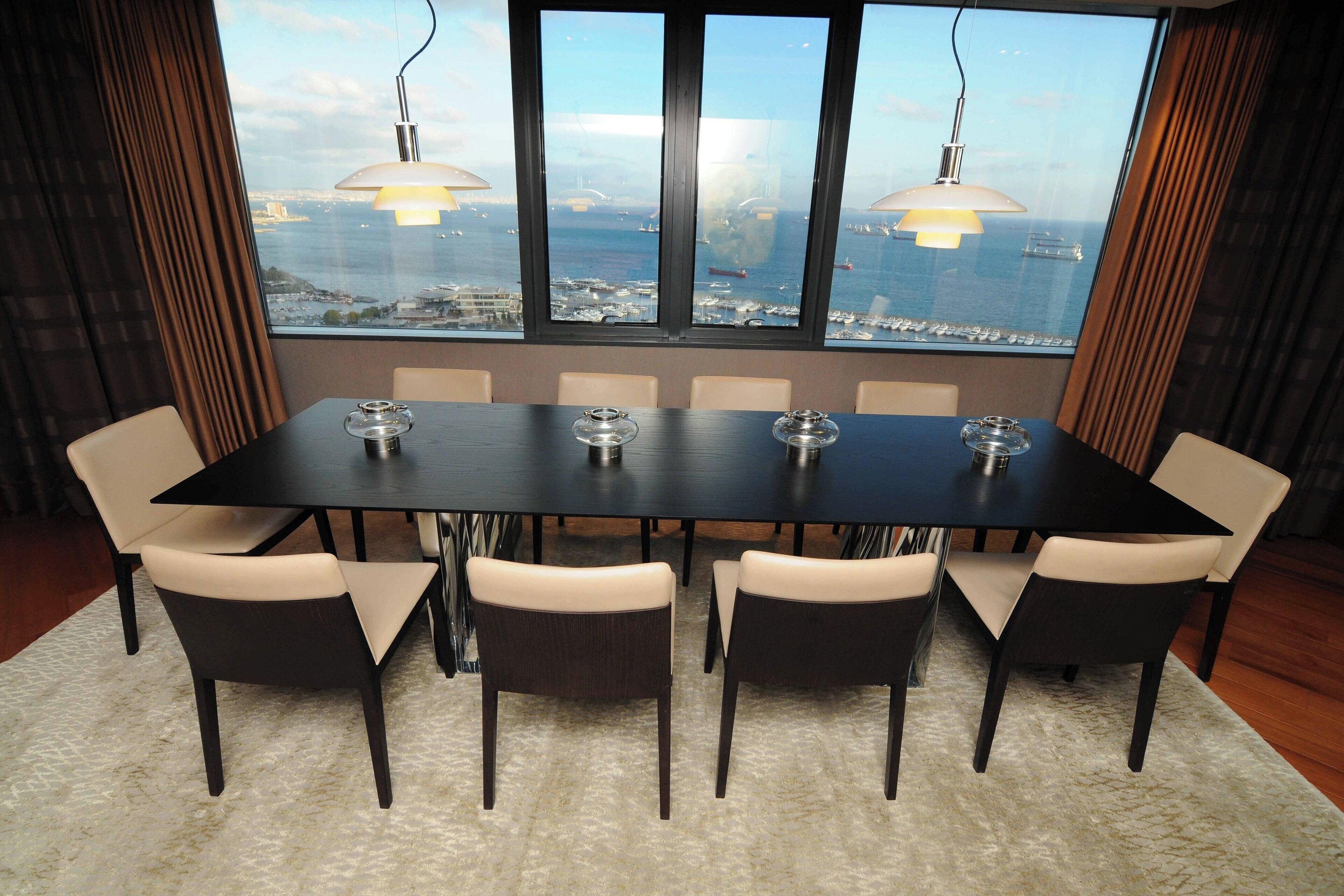 A conference room with a large table and six chairs, large windows with a city and water view, and pendant lighting.