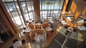 A high-ceilinged dining area with round tables and chairs, large windows offering a view of the outdoors, and a central decorative structure. - Sheraton Istanbul Atakoy Hotel (Istanbul)