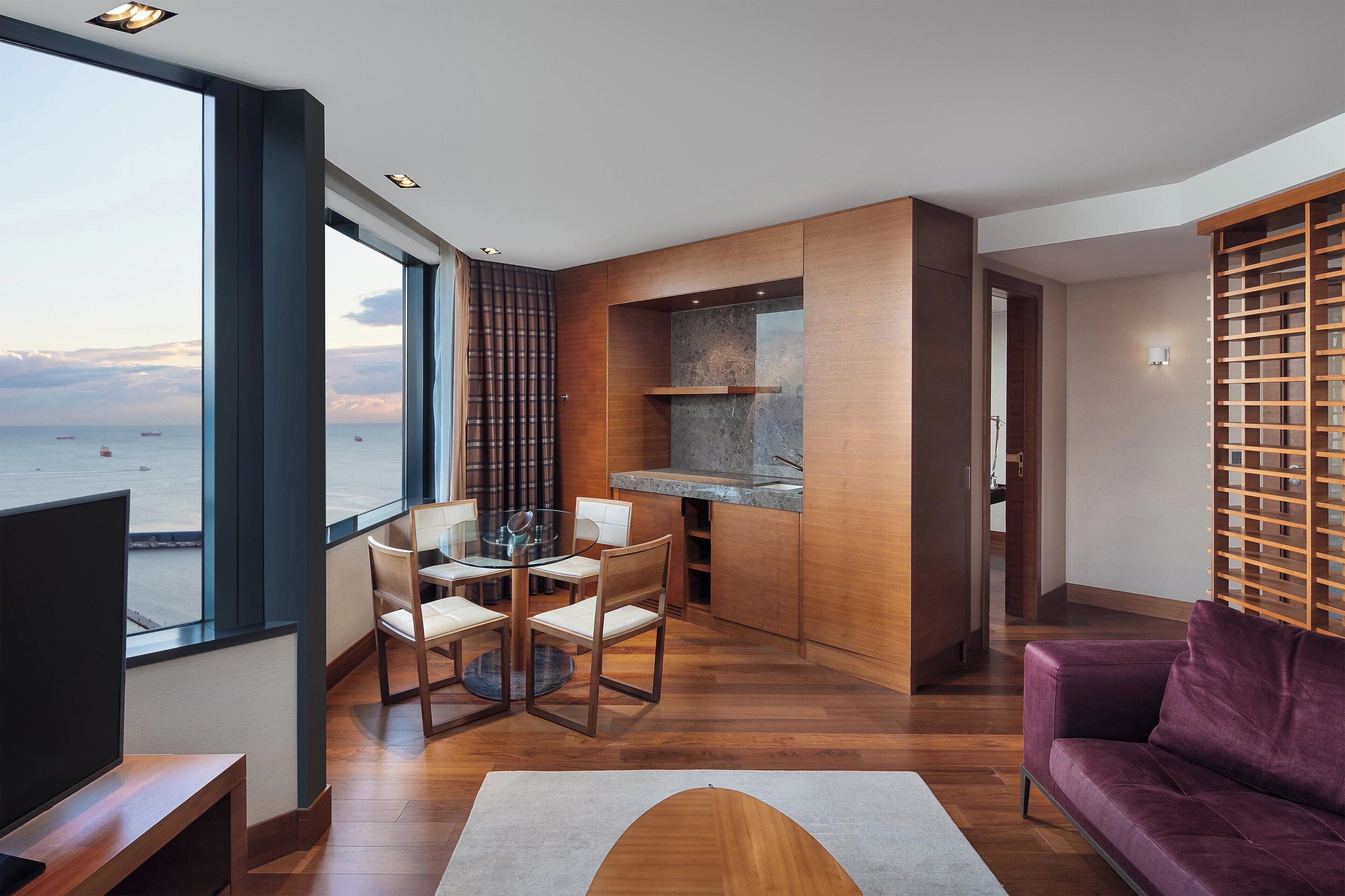 Una sala de estar moderna con un ventanal grande, piso de madera, una mesa de comedor de vidrio y un sofá púrpura.