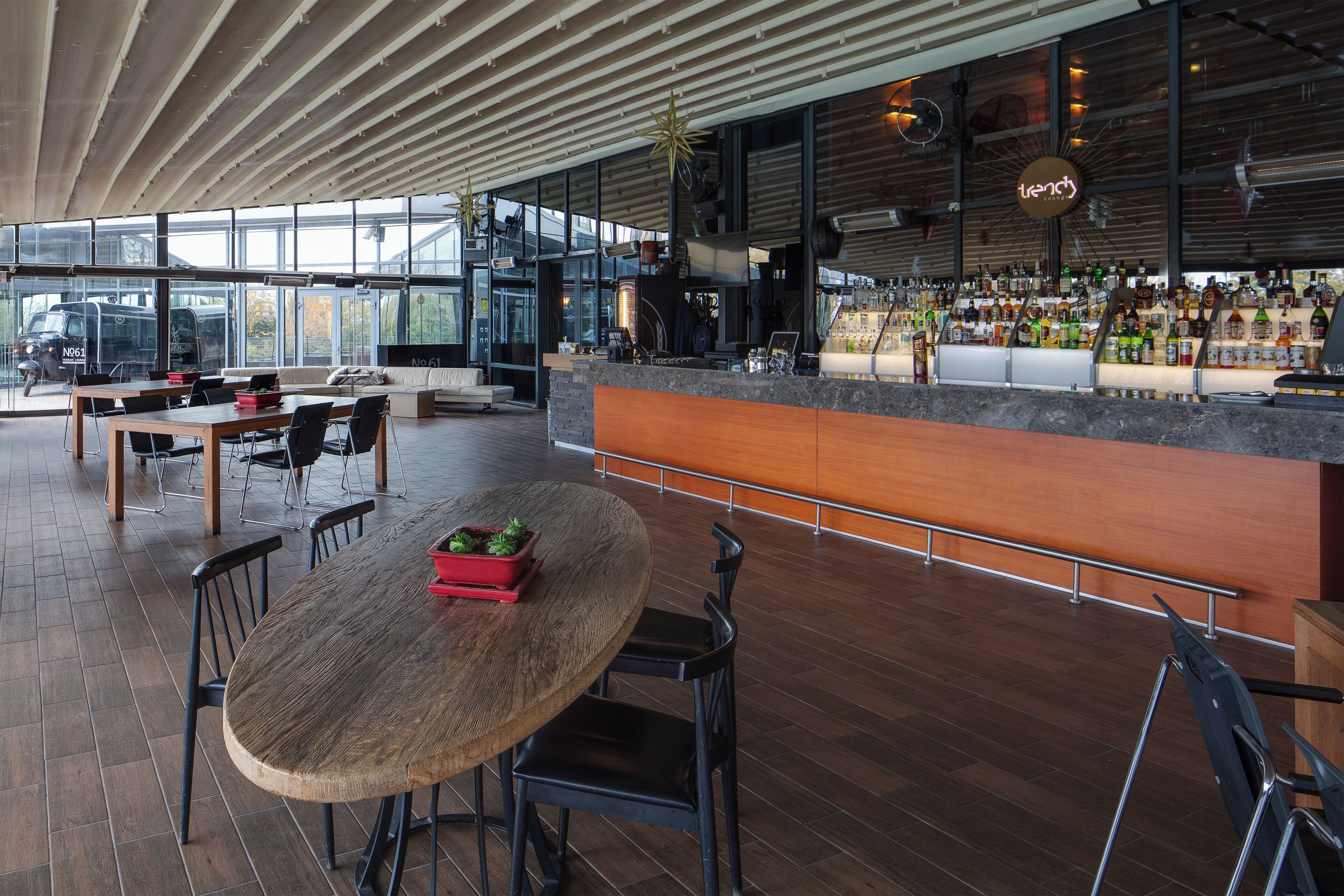 Un moderno bar con una mesa y sillas de madera, una barra repleta de botellas y un amplio ventanal con vistas al exterior.