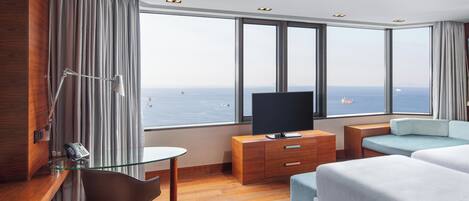 Una habitación de hotel con un ventanal grande, un televisor de pantalla plana, un escritorio con teléfono, una silla, un sofá y una cama.