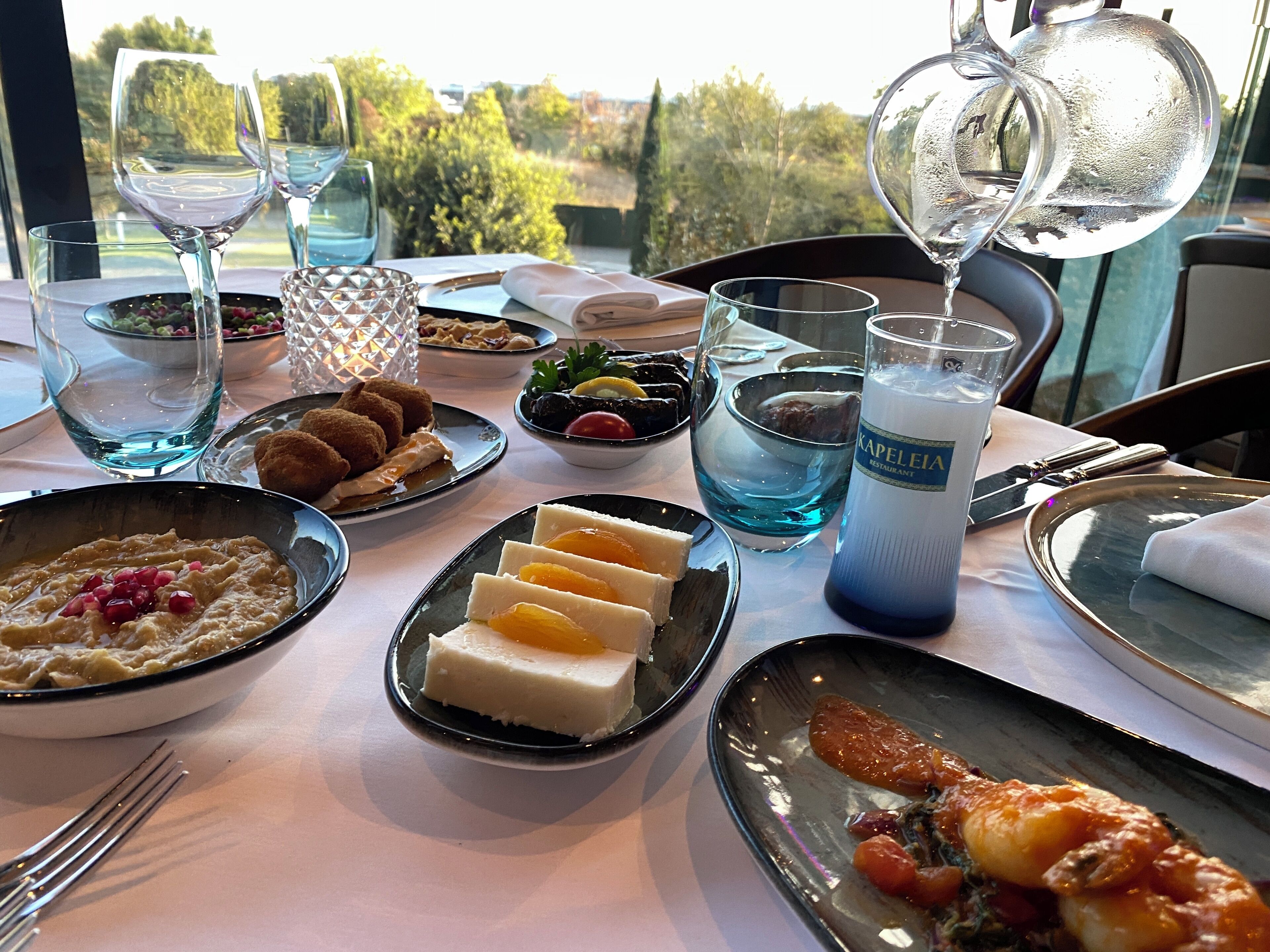 A table set for a meal with various dishes, glasses of water, and a bottle of water labeled "KAPELLEIA".