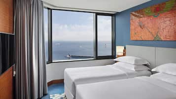 Una habitación de hotel con dos camas, un ventanal con vistas al mar y un cuadro en la pared.