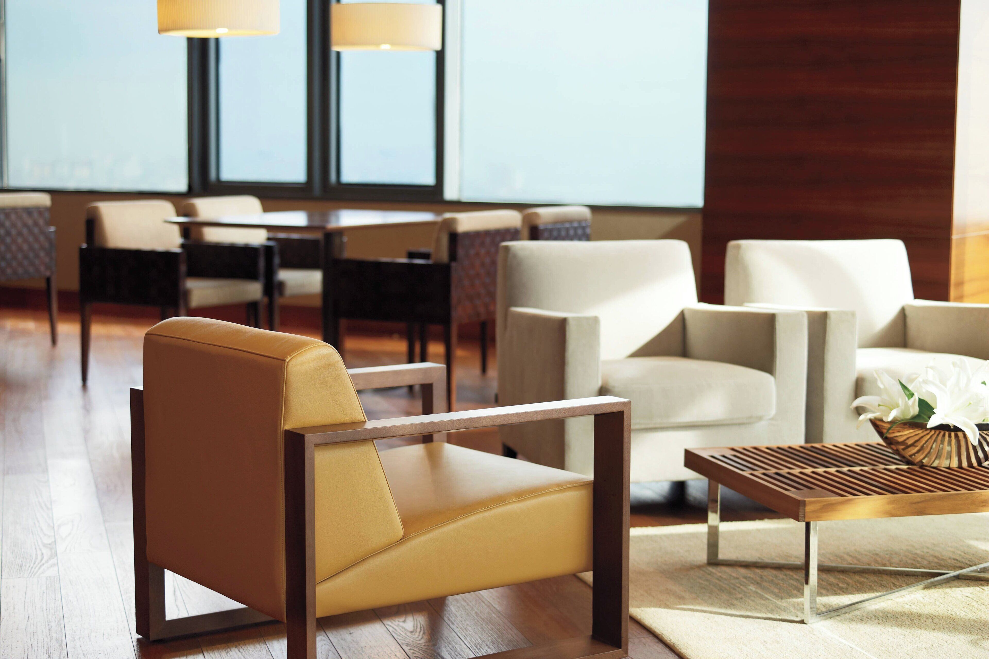 A modern hotel lobby with leather chairs, a wooden coffee table, and a view of the city through large windows.