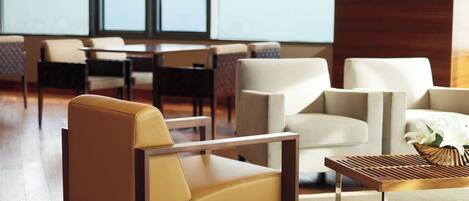Un moderno vestíbulo de hotel con sillones de cuero, una mesa de centro de madera y vistas de la ciudad a través de amplios ventanales.