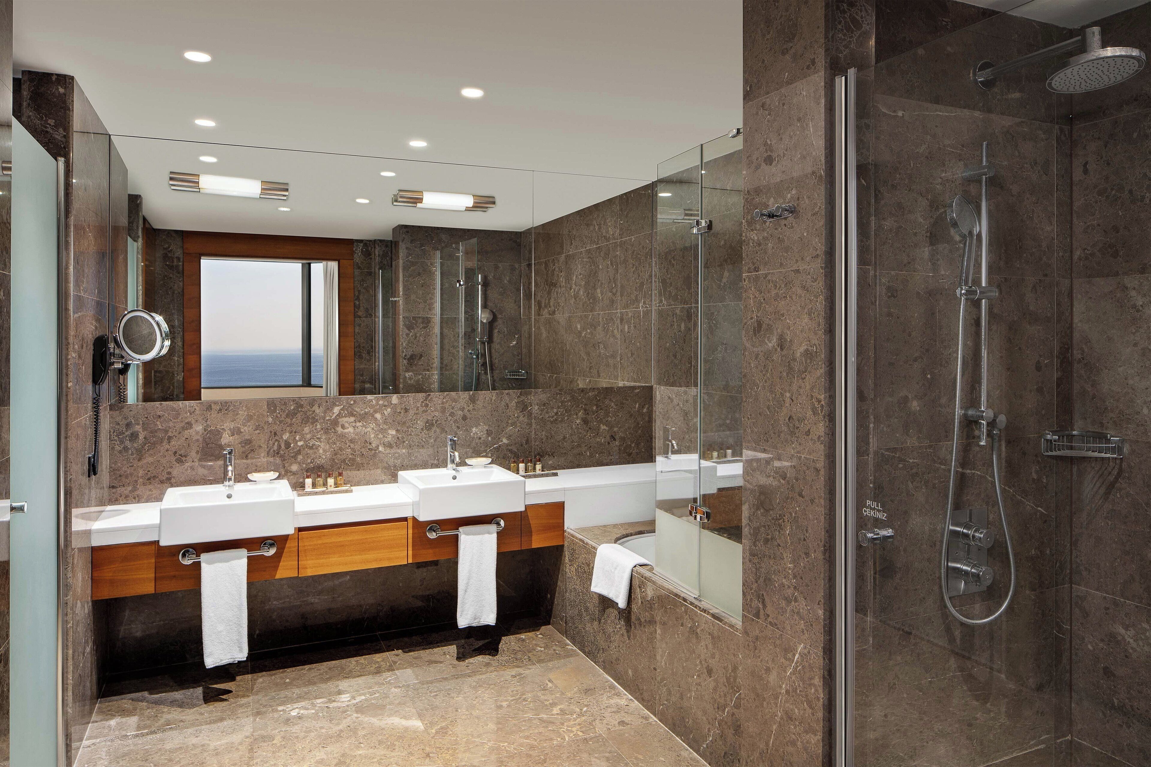 A modern bathroom with two sinks, a large mirror, and a glass-enclosed shower.