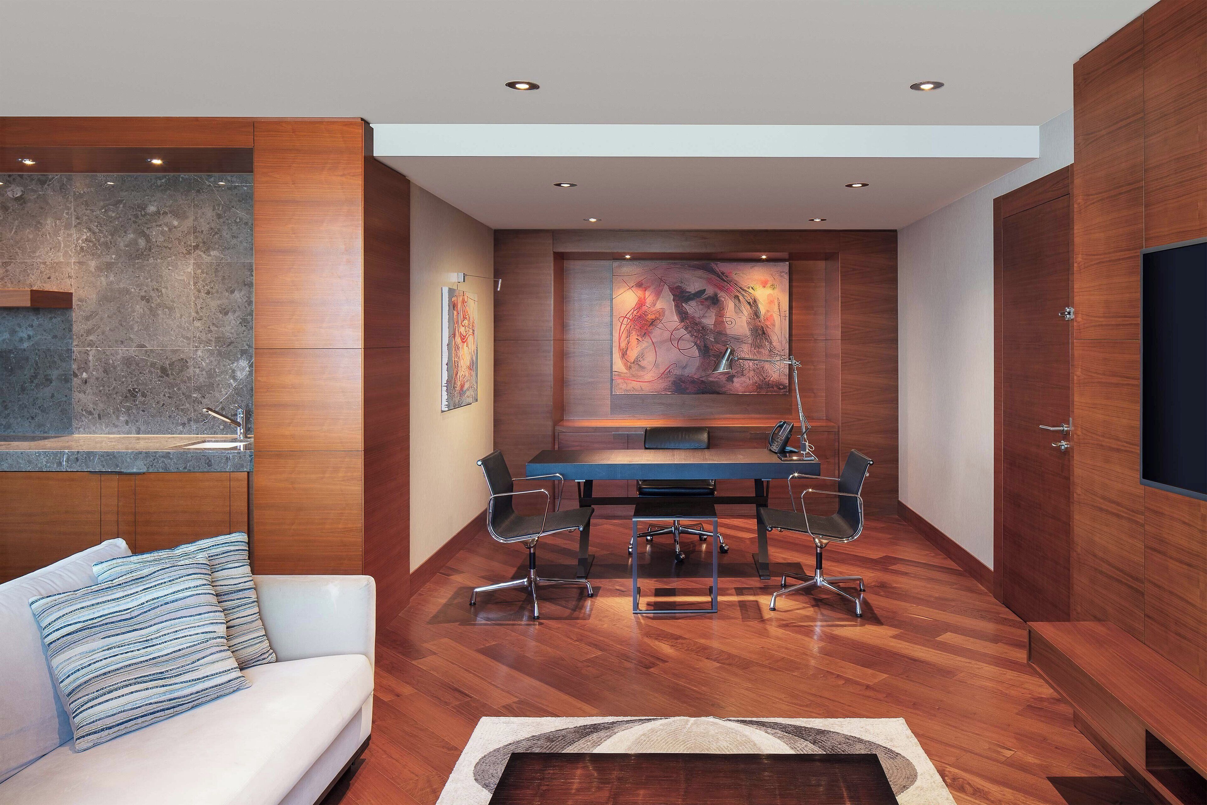 A modern interior with a wooden floor, a white sofa with striped pillows, a glass-top table with chairs, and abstract wall art.