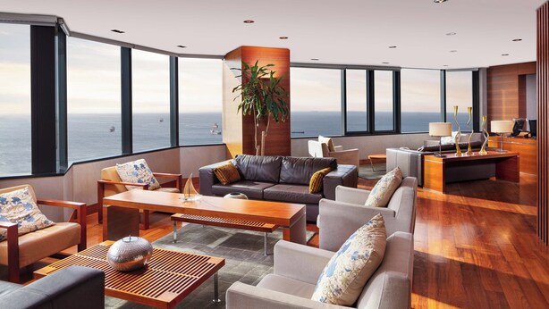 A spacious living area with a large window overlooking the ocean, furnished with sofas, a coffee table, and a plant. - Sheraton Istanbul Atakoy Hotel (Istanbul)
