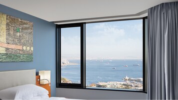Ein Hotelzimmer mit einem großen Fenster und Blick auf das Meer und die Stadt.