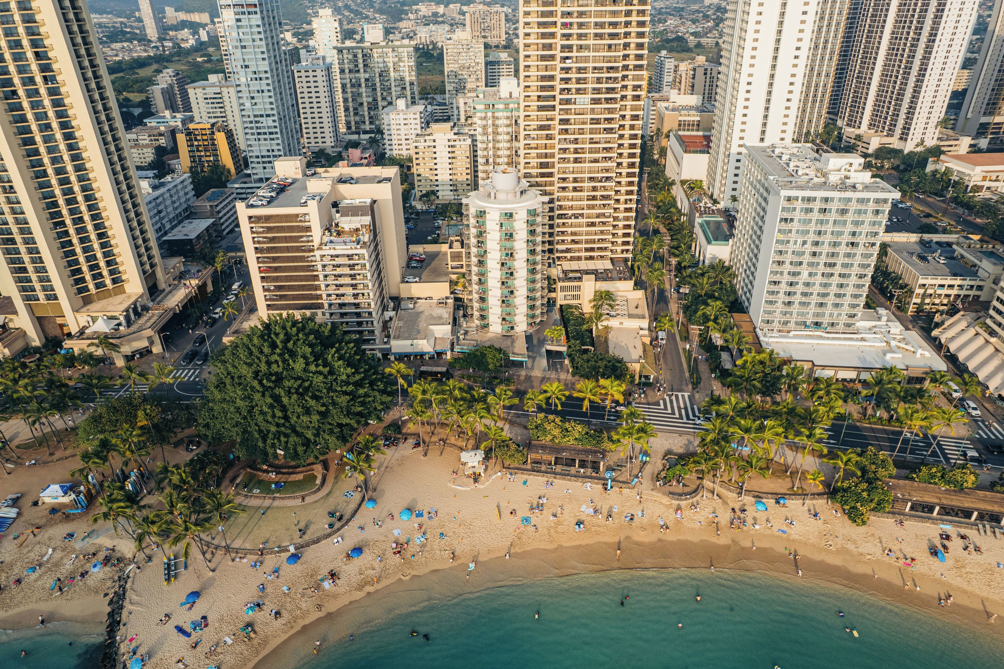 An aerial view of a coastal city with high-rise buildings, a sandy beach, and palm trees.