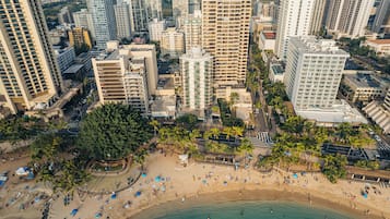 An aerial view of a coastal city with high-rise buildings, a sandy beach, and palm trees.