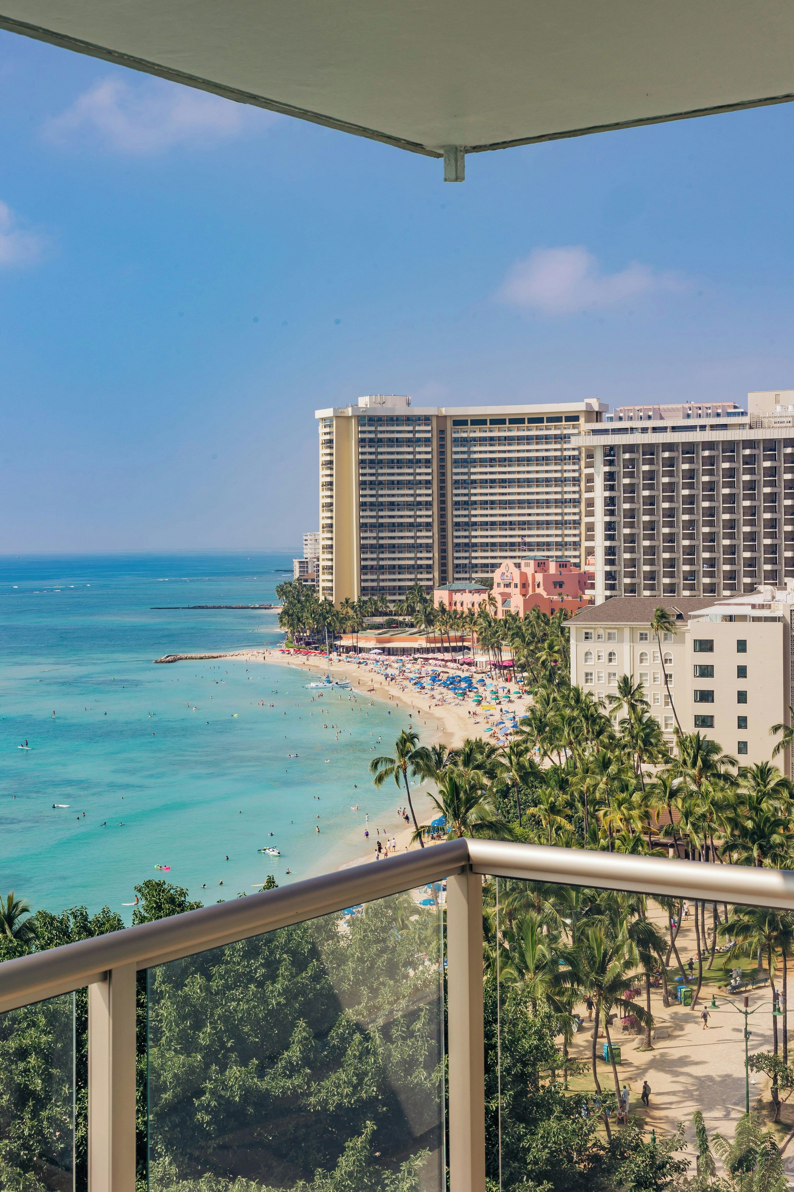 A beachfront hotel with multiple floors, a beach with umbrellas, and palm trees.