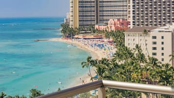 A beachfront hotel with multiple floors, a beach with umbrellas, and palm trees.