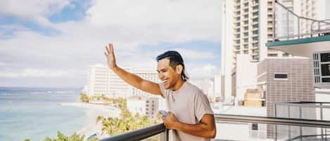 A person standing on a balcony with a view of the ocean and buildings.