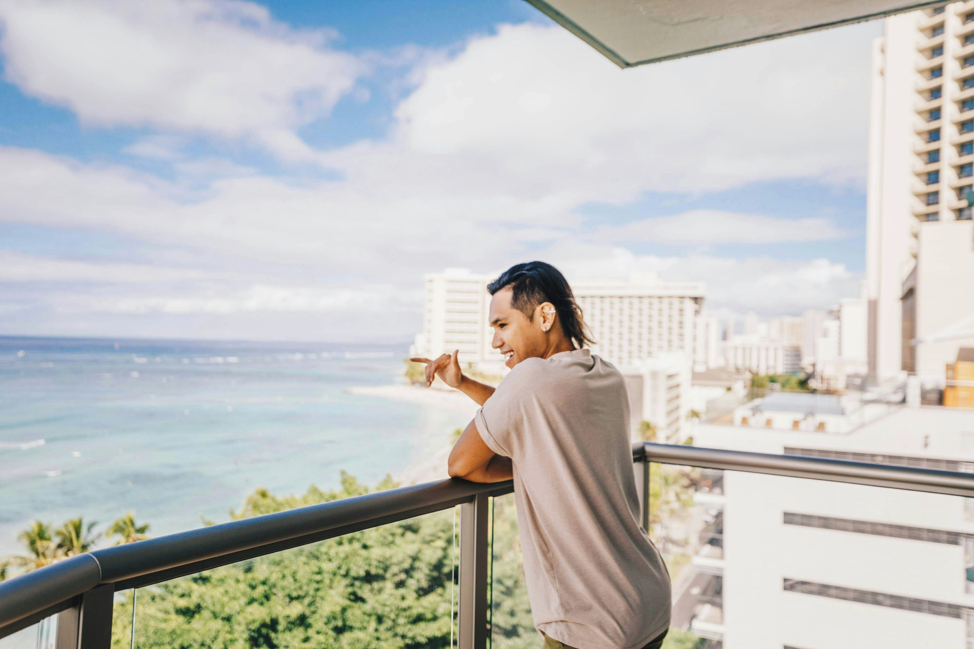 A person standing on a balcony overlooking a cityscape with a view of the ocean.