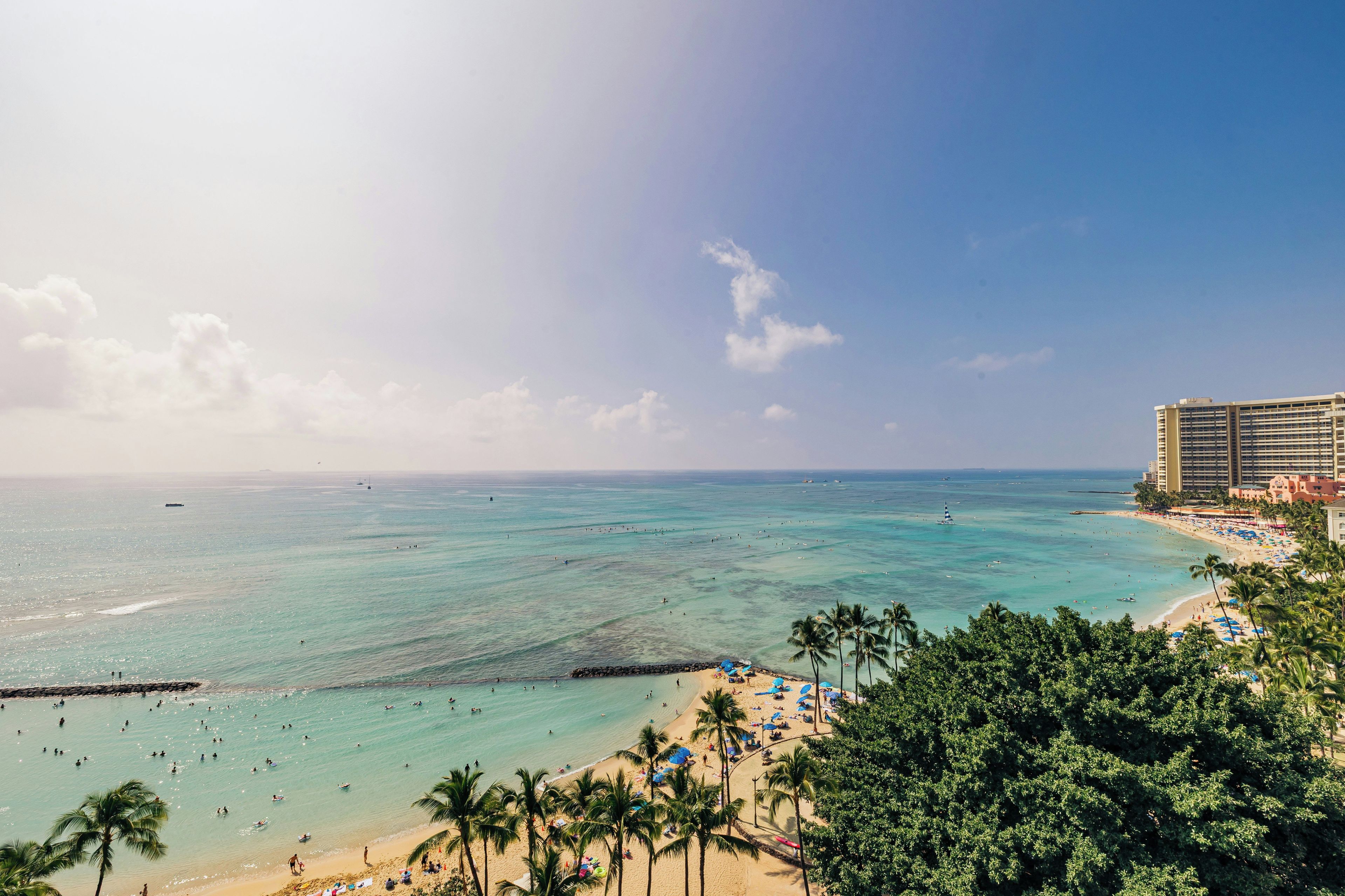 A beach with clear turquoise waters, palm trees, and a hotel in the background.