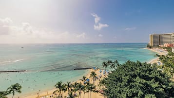 A beach with clear turquoise waters, palm trees, and a hotel in the background.