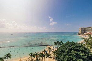 A beach with clear turquoise waters, palm trees, and a hotel in the background.