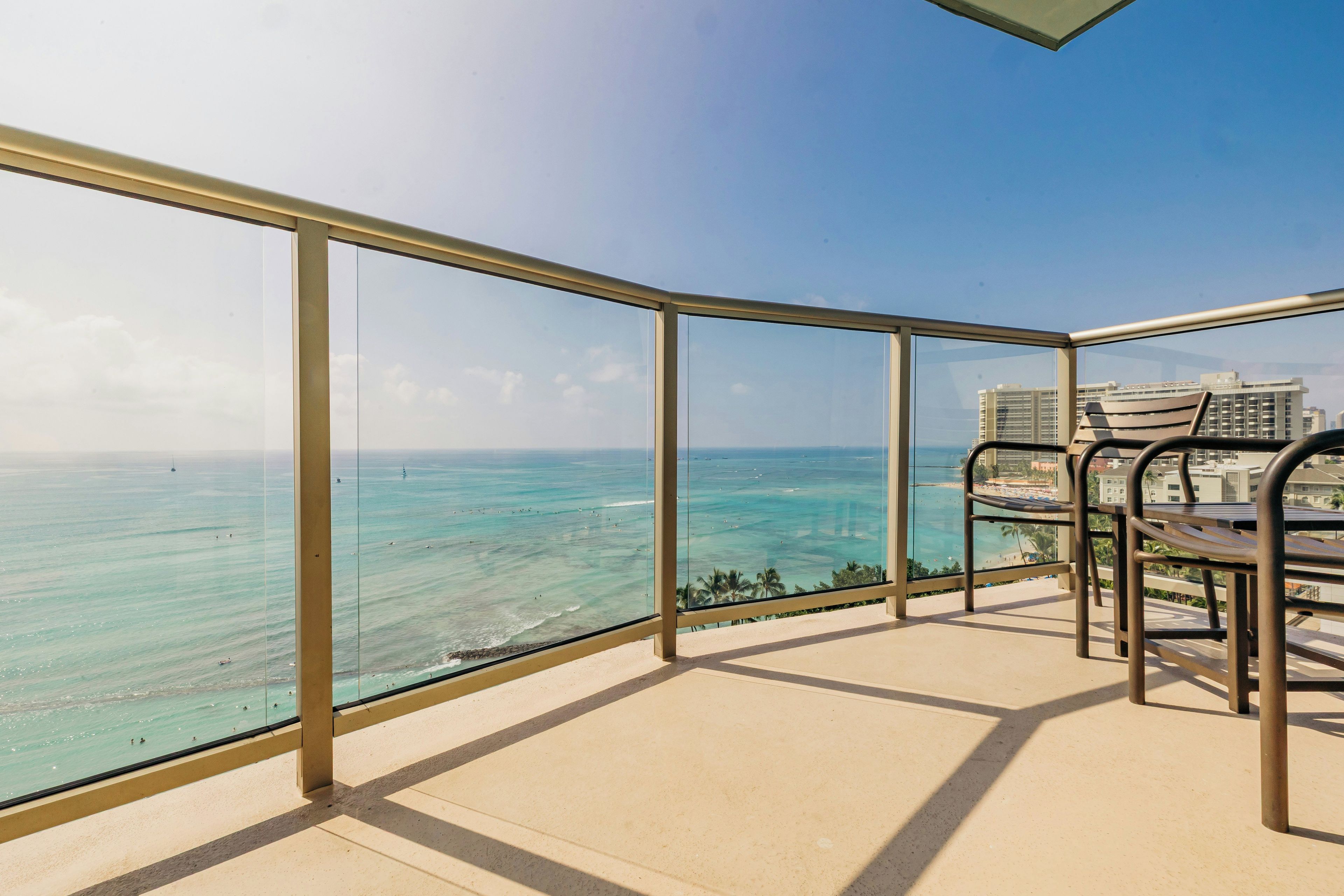 A balcony with a glass railing overlooking a beach and ocean.