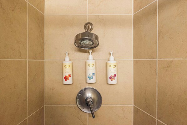 A bathroom with a shower head, three bottles of Hawaiian Tropic products, and a faucet. - Waikiki Circle Hotel By Castle (Honolulu)