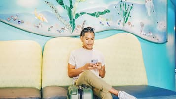 Une personne assise sur un banc, une valise à ses côtés, et qui utilise un téléphone intelligent.