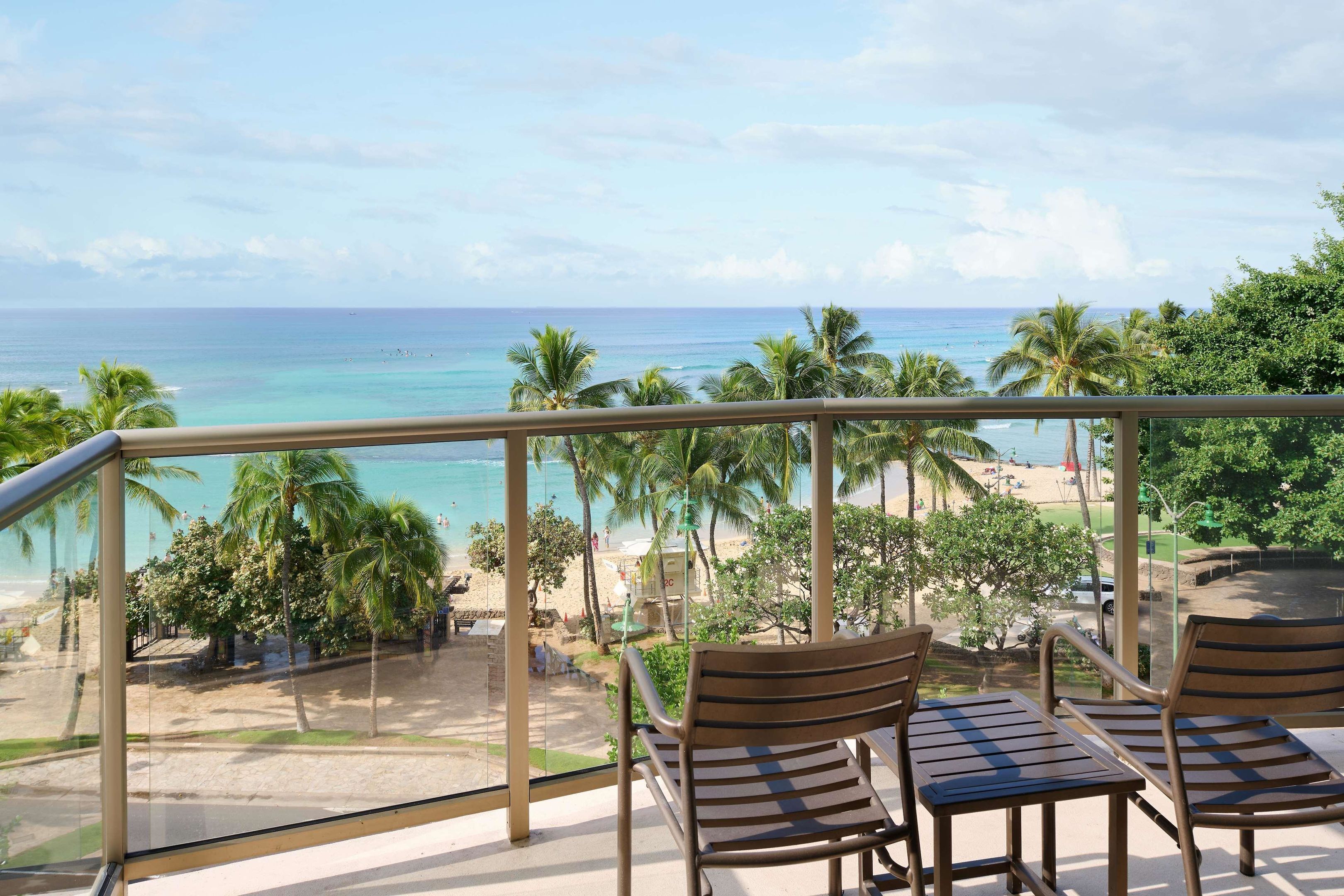 A balcony with a view of the ocean, palm trees, and beach.