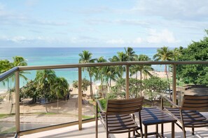 Un balcón con vista al océano, palmeras y la playa.