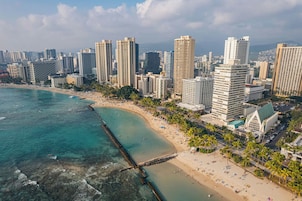 A coastal cityscape with high-rise buildings, a beach, and a pier.