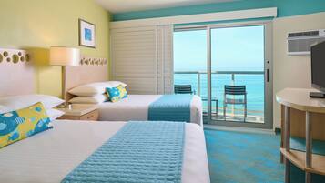 A hotel room with two beds, a desk, a chair, and a balcony with a view of the sea.