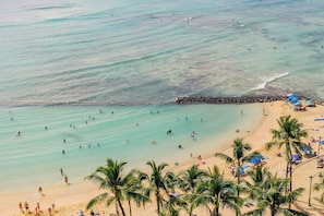A beach with clear turquoise water, palm trees, and people swimming and sunbathing. - Waikiki Circle Hotel By Castle (Honolulu)