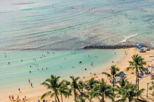 Una playa con aguas turquesas cristalinas, palmeras y gente nadando y tomando el sol.