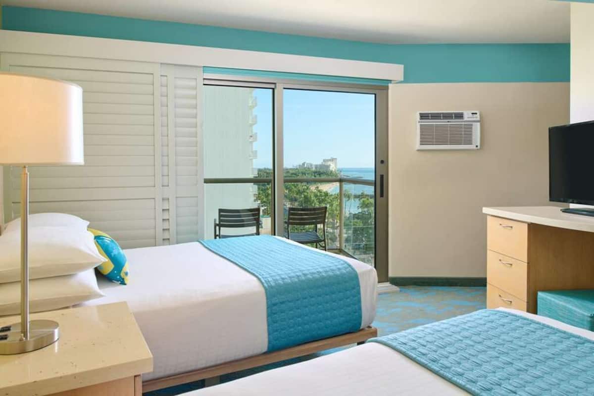 Habitación de hotel con cama, escritorio, televisión y balcón con vistas.