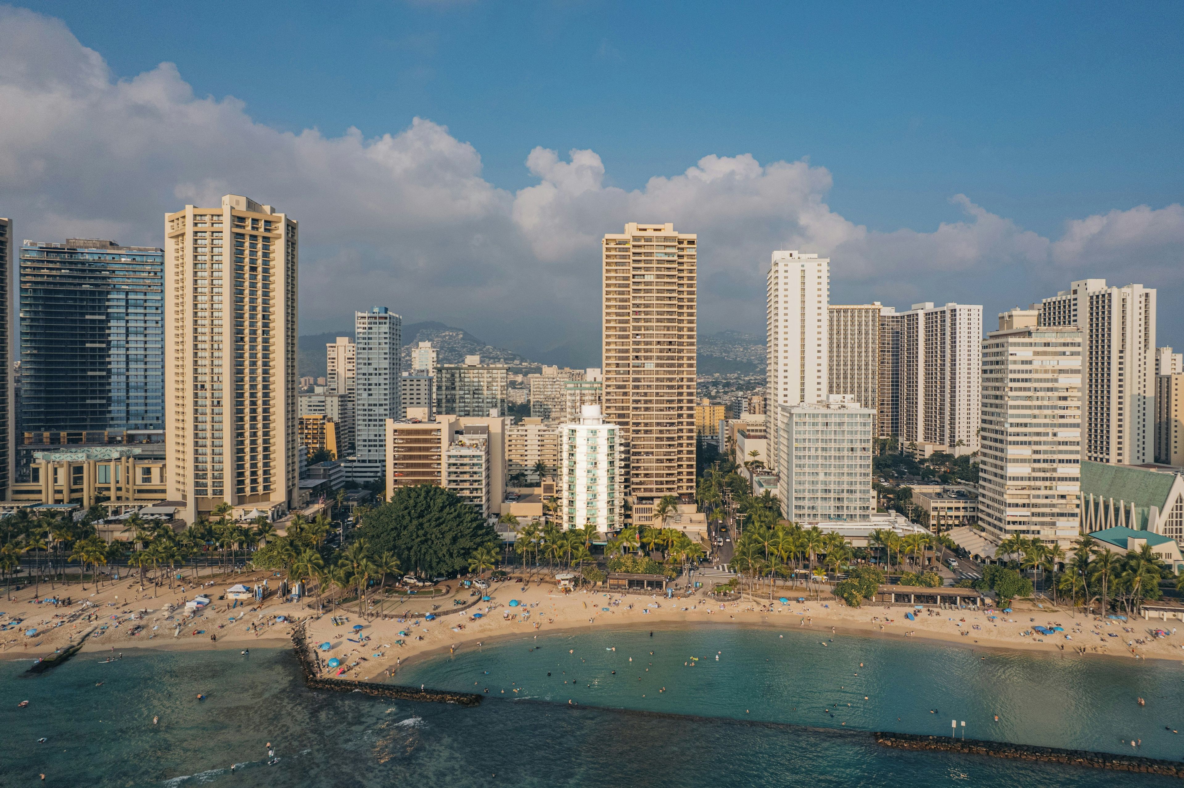 Paisagem costeira com edifícios altos, uma praia de areia e águas azuis cristalinas.