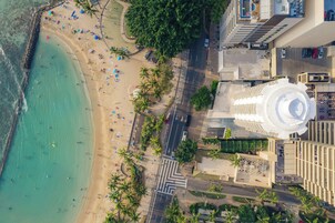 Vista aérea de una playa con palmeras, una carretera y un edificio blanco grande con una cúpula.